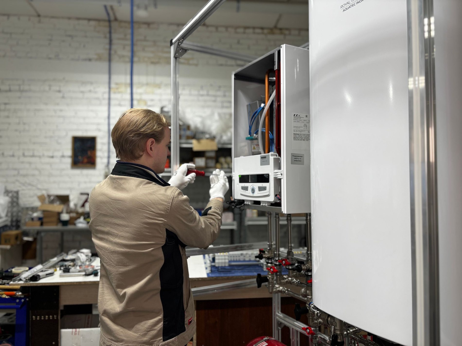 A heating engineer working on a wall-hung boiler beside a hot water cylinder