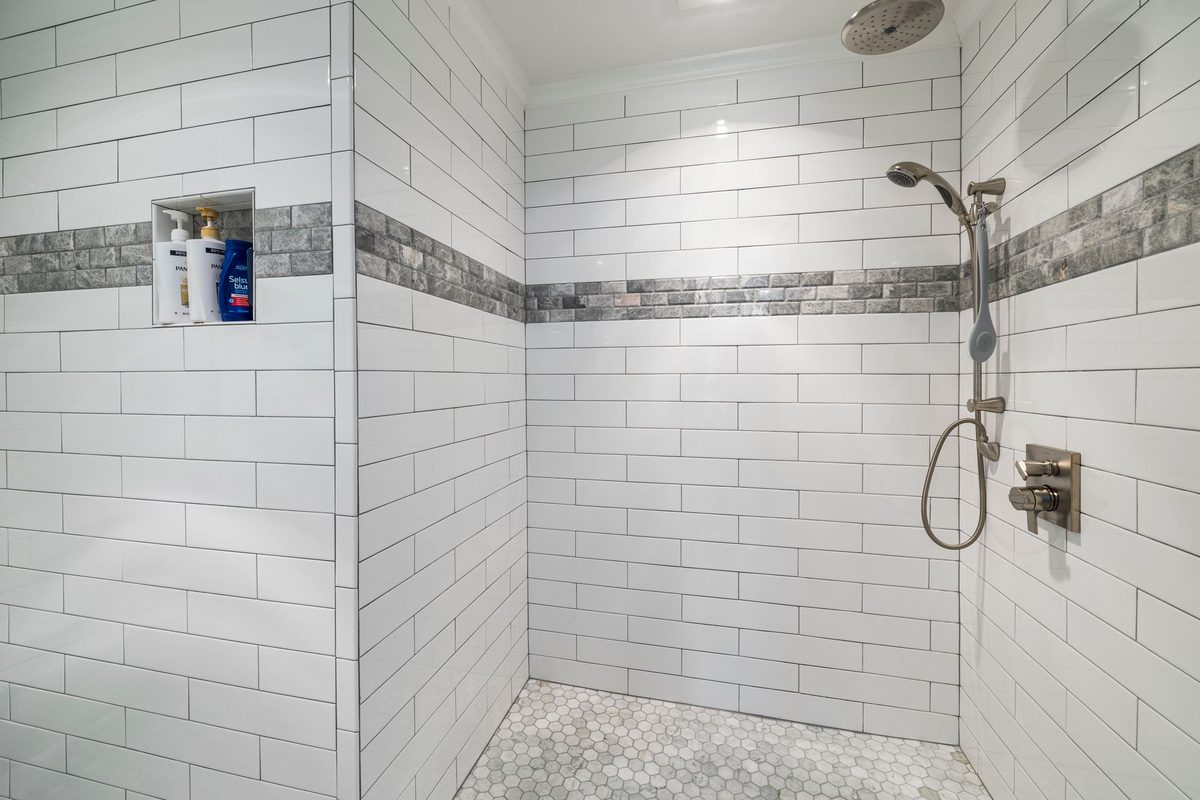 Metro tiling in a shower with a mosaic feature band — the cuts landing where you don't look, full tiles where you do.